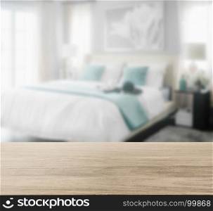 wooden table top with blur of cozy bedroom interior with white and green pillows on bed