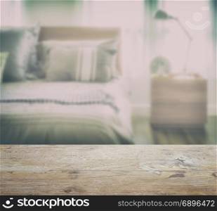 wooden table top with blur of modern bedding with reading lamp in the bedroom