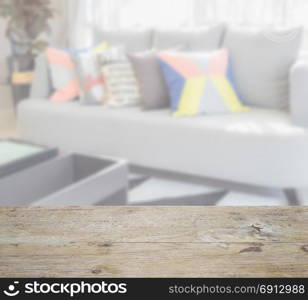 wooden table top with blur of modern living room design with colorful pillows on sofa