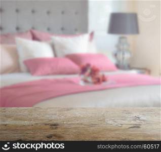 wooden table top with blur of red bed and pillows in modern bedroom as background