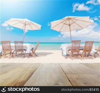 wooden table top with blur of table set and umbrella on the beach