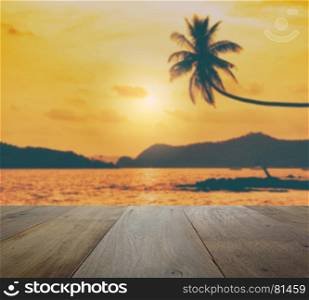 wooden table top with blurred coconut tree hanging over the tropical beach at sunset