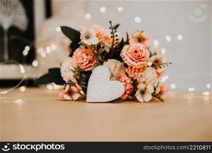 wooden table with a bouquet of flowers and a white heart and bokeh lights around it.