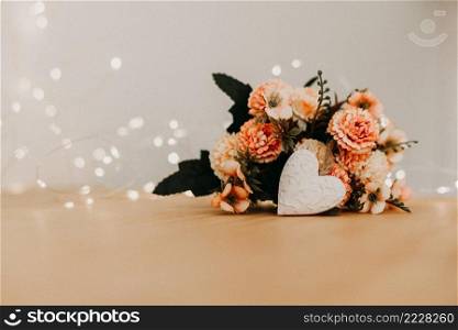 wooden table with a bouquet of flowers and a white heart and bokeh lights around it.
