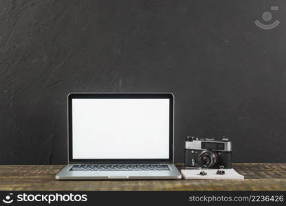 wooden table with blank screen laptop retro camera black background