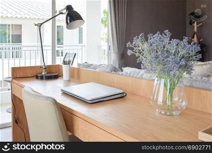 wooden table with computer notebook,pencil,lamp and artificial flowers in modern working area at home