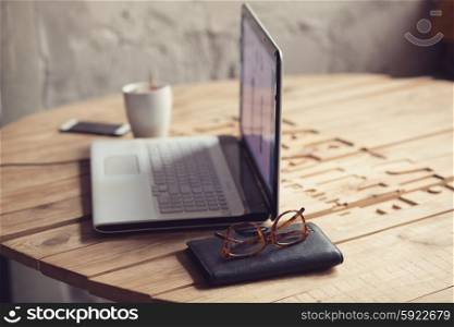 Wooden table with laptop, glasses, wallet and cup of coffee