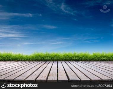wooden terrace with fresh spring green grass and blue sky