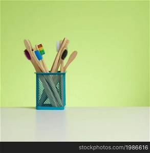 wooden toothbrushes in a plastic cup on a white table. Green background, zero waste. Copy space