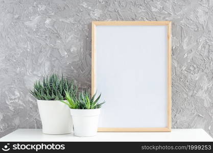 Wooden vertical white empty frame and two natural succulents flowers in white pots on table on gray concrete wall background. Mockup Template for your design.. Wooden vertical white empty frame and two natural succulents flowers in white pots on table on gray concrete wall background. Mockup Template for your design