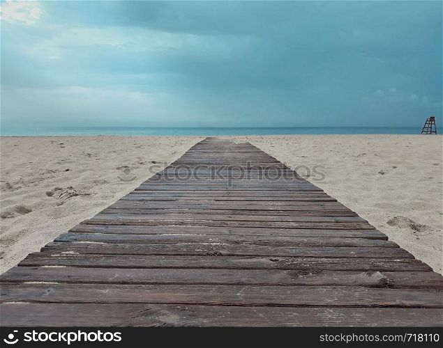 Wooden walkway leading from the beach to the sea with an intense blue sky.