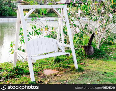 Wooden white swing on the grass of rural village.