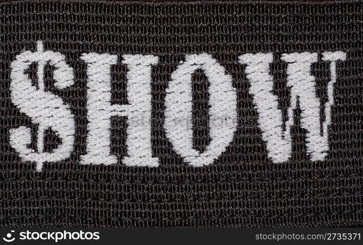 Word &acute;show&acute; embroidered in white thread on black fabric. Shoot close-ups.