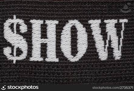 Word &acute;show&acute; embroidered in white thread on black fabric. Shoot close-ups.
