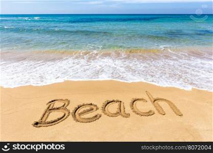 Word Beach written in sand of coast at sea