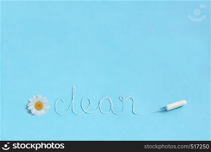 Word CLEAN from white thread hygienic female tampon and chamomile on blue background. Concept hygiene and health women and adolescents during menstrual cycle. Flat Lay, copy space. Word CLEAN from white thread hygienic female tampon and chamomile on blue background.