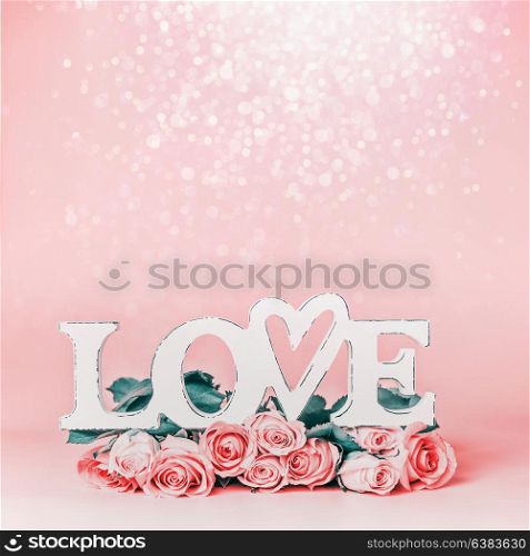 Word LOVE on pastel pink background with lovely roses bunch and bokeh , front view. Creative female holidays layout with copy space for greeting