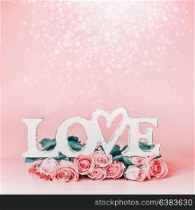 Word LOVE on pastel pink background with lovely roses bunch and bokeh , front view. Creative female holidays layout with copy space for greeting