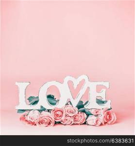 Word LOVE on pastel pink background with lovely roses bunch, front view. Creative female holidays layout with copy space for greeting