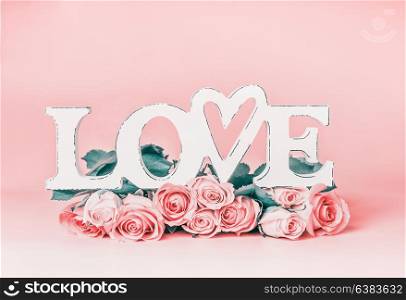 Word LOVE on pastel pink background with roses bunch, front view. Creative female holidays layout with copy space for greeting