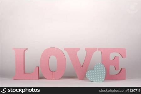 word love with pink cork letters and a small cardboard box in the shape of a heart on a white background. valentine&rsquo;s day concept