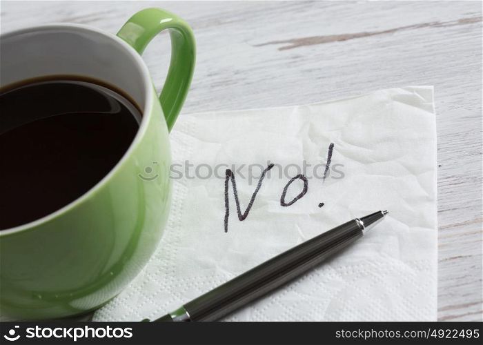 Word NO on napkin. No answer written on napkin and coffee cup on wooden table
