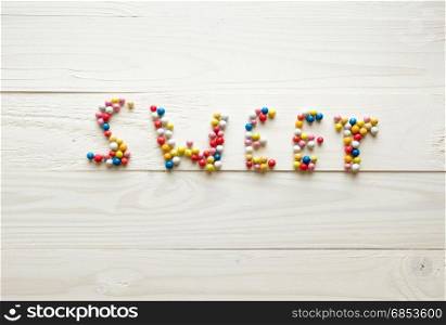 Word Sweet made of colorful round candies on white wooden background
