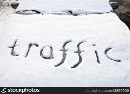 Word traffic written in snow on hood of car during winter season