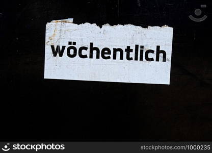 word wochentlich written in German language on a white sign on black dirty, scratched background, translated weekly