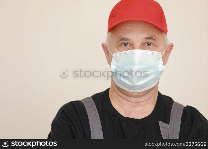 Work are done. Portrait of worker man with medical mask in red overall, black t shirt , red cap looking in camera. white background, indoor studio shoot isolated. Work are done. Portrait of worker man with medical mask in red overall, black t shirt , red cap looking in camera. white background, indoor studio shoot isolated.