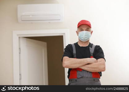 Work are done. Portrait of worker man with medical mask in red overall, black t shirt , red cap, standing and folded arms. white background, indoor studio shoot isolated. Work are done. Portrait of worker man with medical mask in red overall, black t shirt , red cap, standing and folded arms. white background, indoor studio shoot isolated.