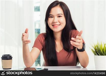Work from home, Asian business young beautiful woman smiling sitting on desk workspace raise hand explain job communication with team video conferencing on digital tablet computer at home office
