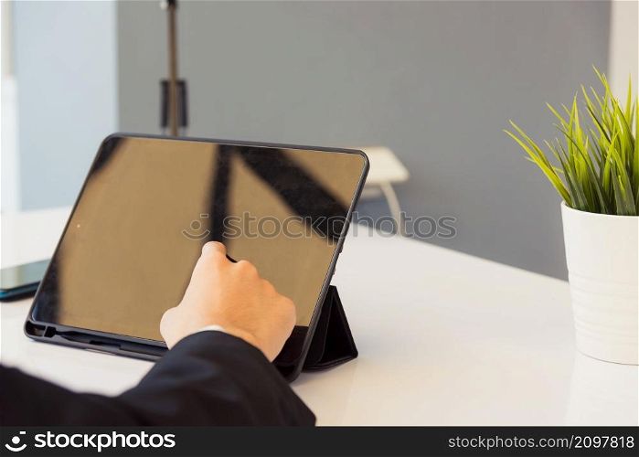 Work from home, Back view of Asian young businessman smile wearing suit video conference call or facetime by smart digital tablet computer he use finger touch on blank screen of tablet on desk