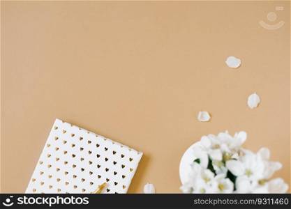 Work from home concept apartment lay on beige table with notepad, pen and vase of flowers. View from above. Copy space