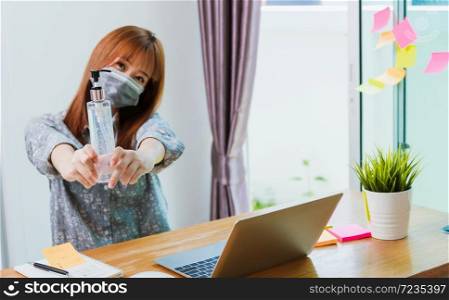 Work from home concept, Asian young business woman wearing face mask protective quarantines disease pandemic coronavirus or COVID-19 her show sanitizing gel with laptop computer at home office