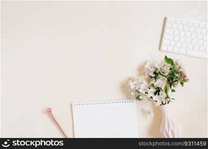 Work from home concept flat lay on beige table with notepad, pen, keyboard and vase of flowers. View from above. Copy space