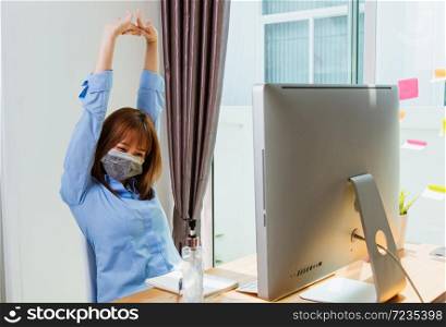 Work from home concept, Happy Asian beautiful young business woman wearing face mask protective quarantines disease coronavirus or COVID-19 her stretching her arms above her head after success work