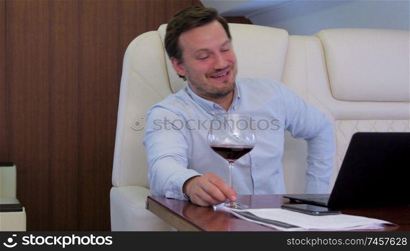 Work on laptop on board of private jet. Businessman comfortably discussing with partner while drinking wine inside of business airplane cabin.. Two businessmen comfortably work on private plane