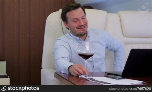 Work on laptop on board of private jet. Businessman comfortably discussing with partner while drinking wine inside of business airplane cabin.. Two businessmen comfortably work on private plane