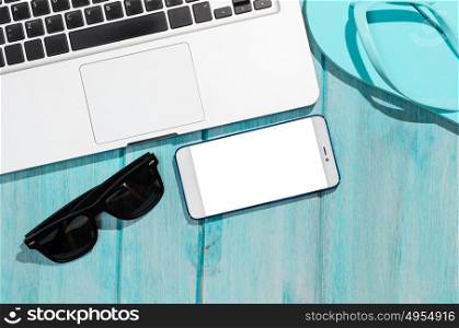 Work on the go. Modern laptop computer with smartphone and sunglasses on blue table, view from above