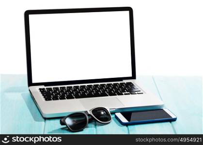 Work on the go. Modern laptop computer with smartphone and sunglasses on blue table