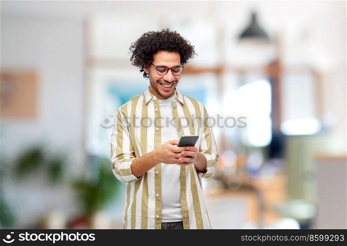 work, people and technology concept - happy smiling man in glasses with smartphone over office background. happy smiling man in glasses with smartphone