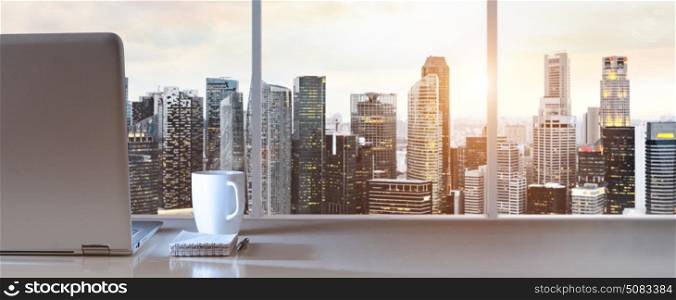Work place with panoramic view. Laptop on table in office with panoramic sunset view of modern downtown skyscrapers at business district