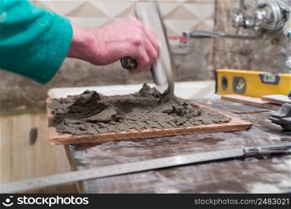 Worker applies cement adhesive on the tiles. Finishing works, blurred focus. The technology of laying tile.. Repair and finishing works