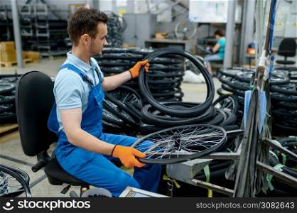 Worker at the assemly line holds bicycle tire on factory. Bike wheels production in workshop, cycle parts installation, modern technology. Worker at the assemly line holds bicycle tire