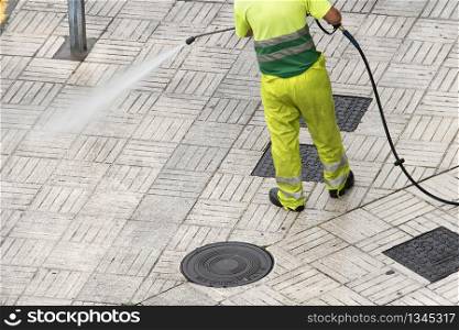 Worker cleaning the street sidewalk with high pressure water jet. Public maintenance concept