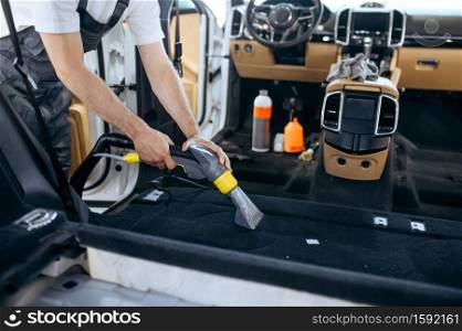 Worker cleans car interior with vacuum cleaner, car dry cleaning and detailing. Vehicle washing in garage, thoroughly care of automobile. Worker cleans car interior with vacuum cleaner