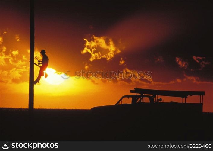 Worker Climbing a Telephone Pole at Sunset