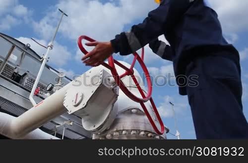 worker closes ball valve on cooling installations at gas compressor station, against background of cloudy sky, closeup