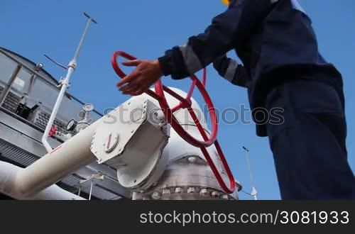 worker closes ball valve on cooling installations at gas compressor station, against background of blue sky, closeup